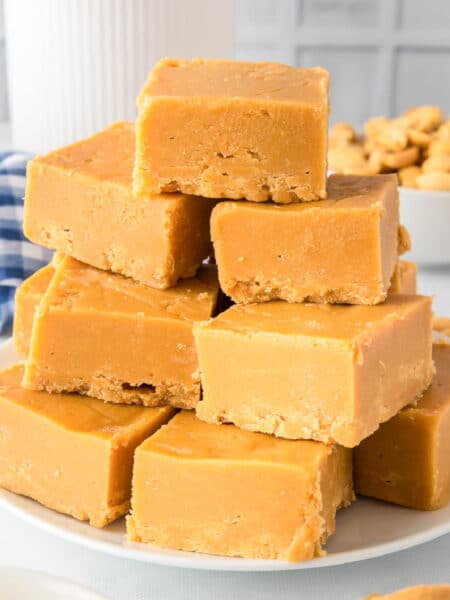 A stack of 2 ingredient peanut butter fudge squares on a plate stacked high from the side on a counter.