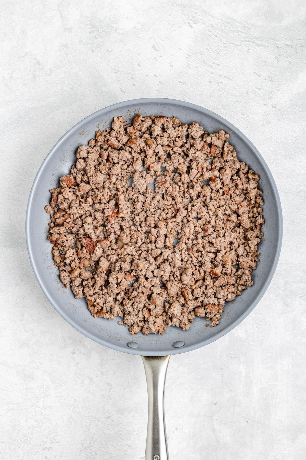 A pan filled with cooked ground sausage for a breakfast biscuit casserole.