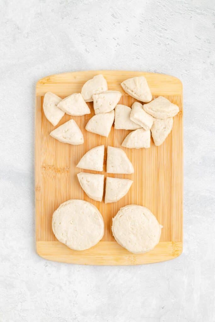 Biscuit dough on a wooden cutting board being cut into quarters for breakfast biscuit casserole.