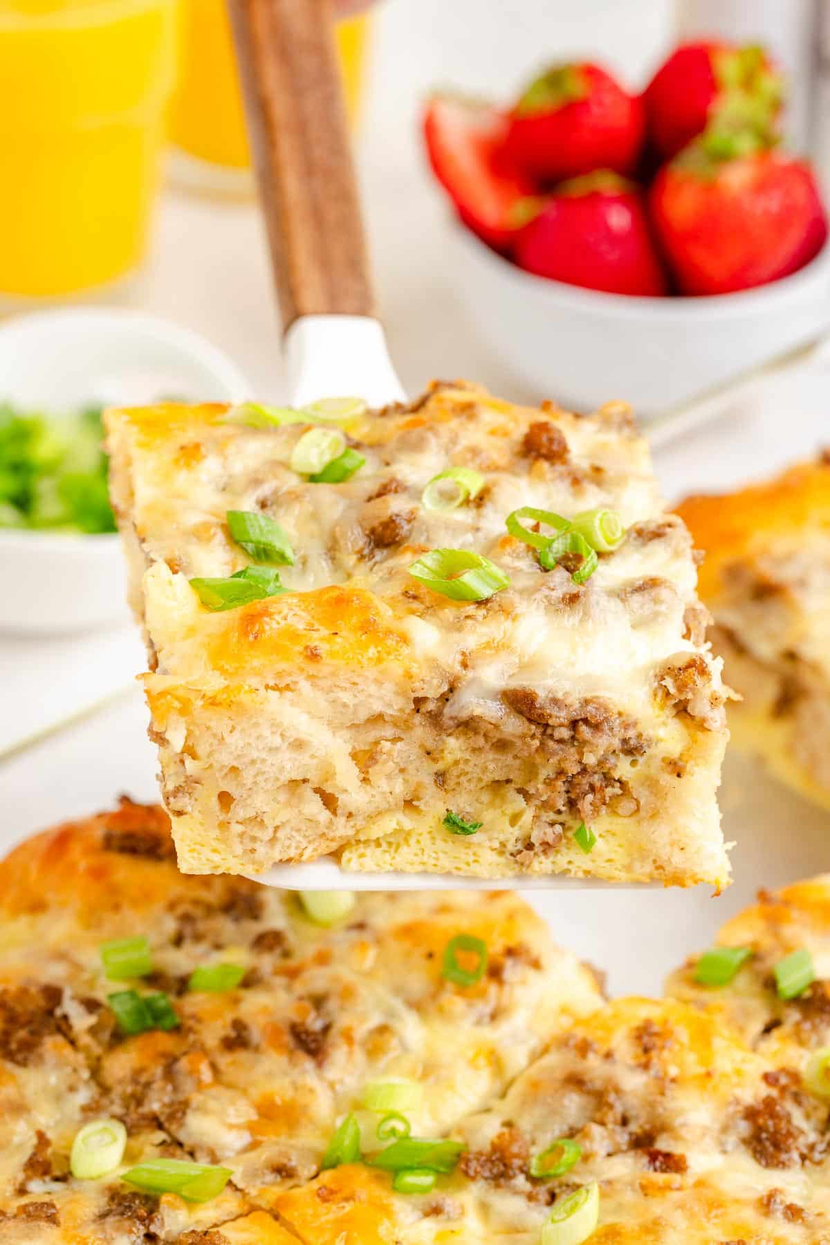 Close-up of a slice of breakfast biscuit casserole with sausage, cheese, and eggs being held above the baking dish as it is removed from the pan.