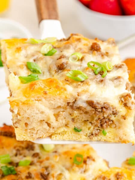 A slice of breakfast biscuit casserole with sausage, egg and cheese being lifted from the casserole pan.