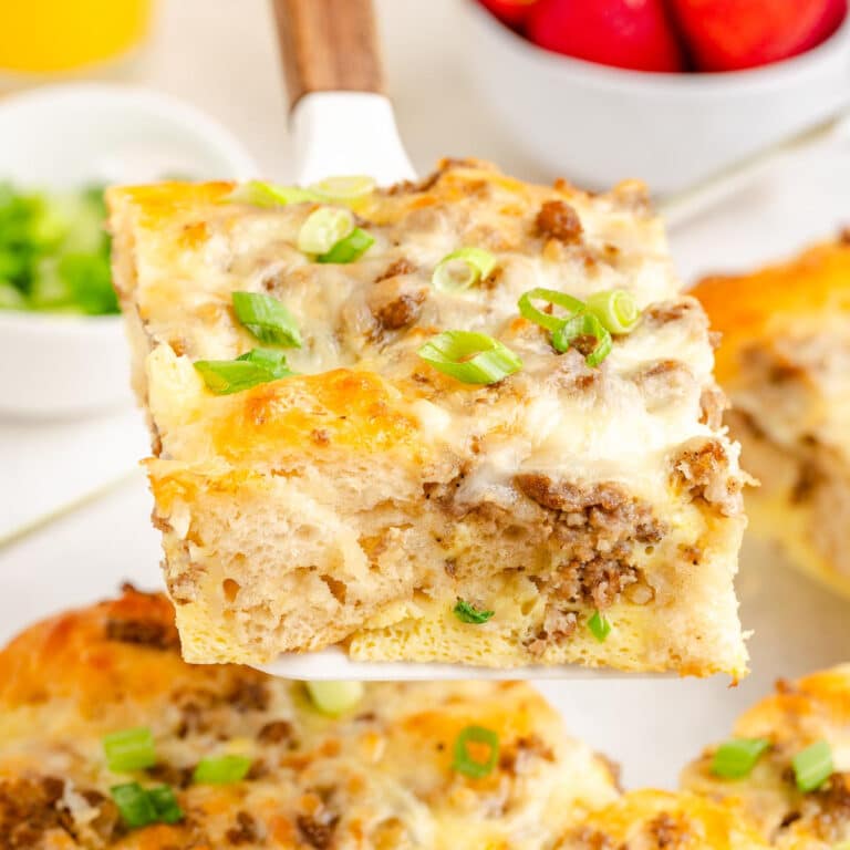 A slice of breakfast biscuit casserole with sausage, egg and cheese being lifted from the casserole pan.