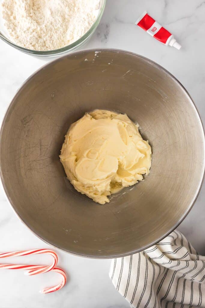 A mixing bowl with the creamed butter mixture and dry ingredients and a tube of red food coloring nearby.