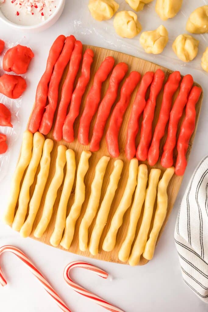 Red and uncolored cookie dough pieces on a cutting board ion rows before twisting them into candy cane cookies.