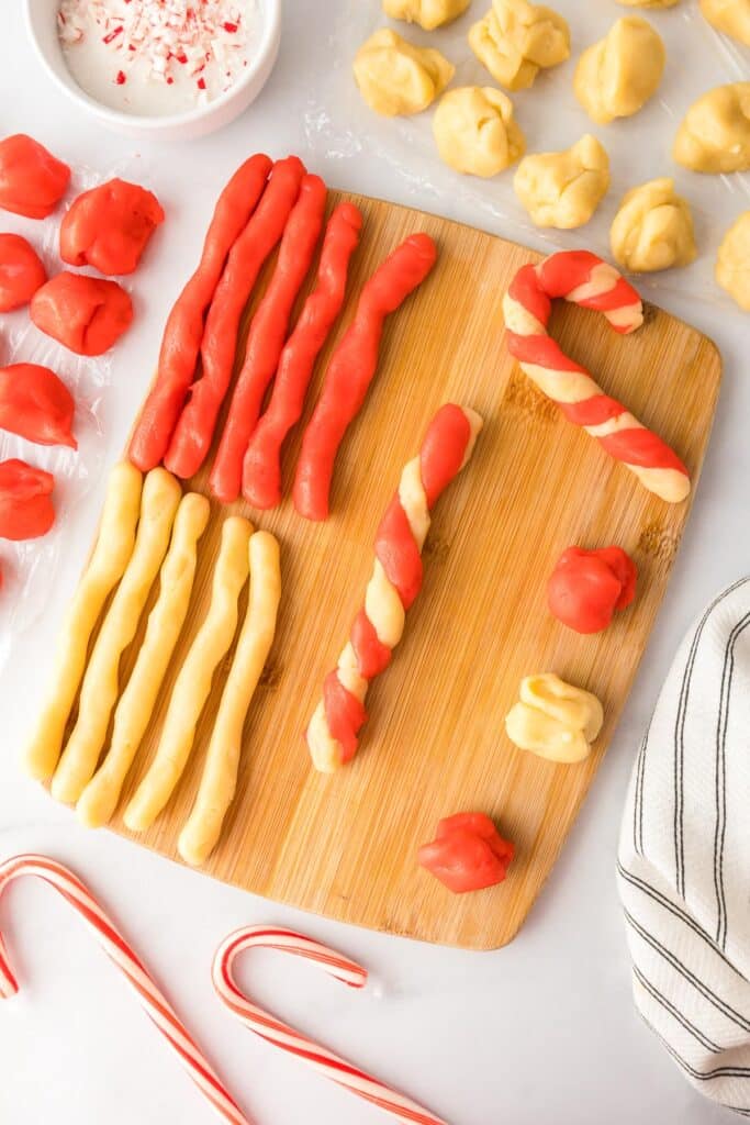 Cookie dough in red and natural dough color in long ropes being twisted into candy canes.