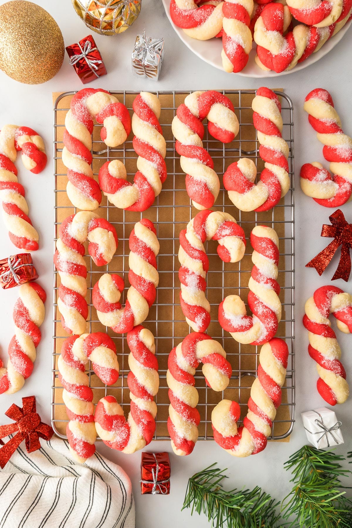 Red and white candy cane cookies on a cooling rack with small holiday decorations nearby.