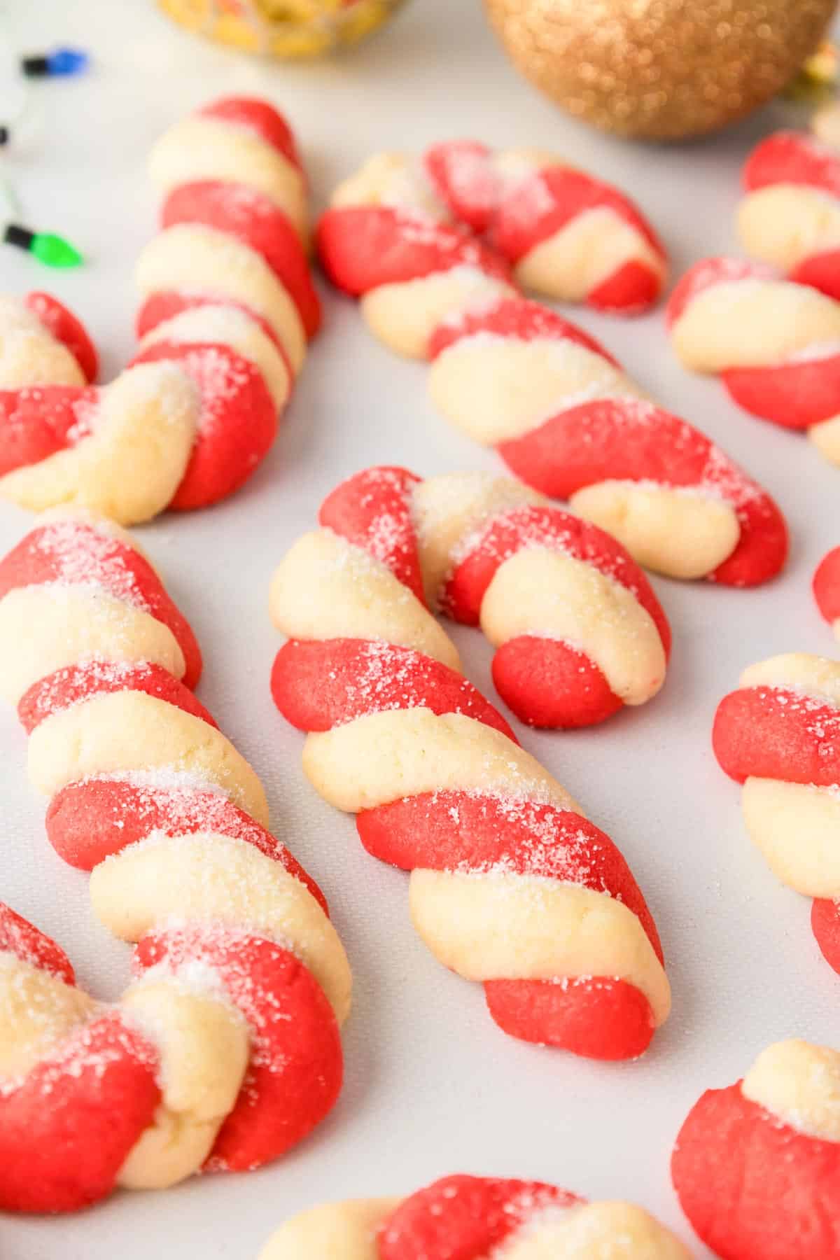 Several twisted red and white candy cane cookies close up on a counter sprinkled with sugar.