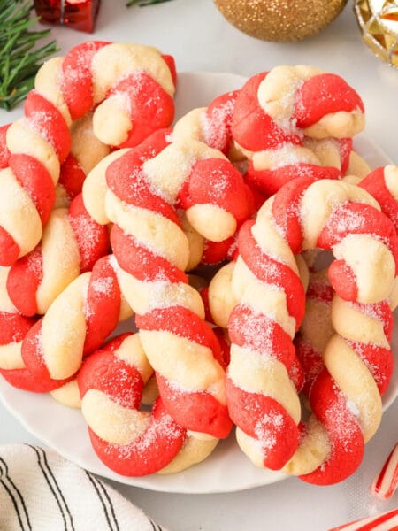 Square view of a plate full of red and white twisted candy canes cookies shaped like candy canes and sprinkled with sugar.