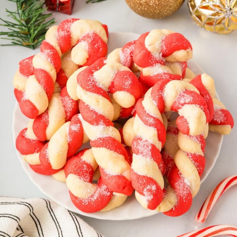 Square view of a plate full of red and white twisted candy canes cookies shaped like candy canes and sprinkled with sugar.