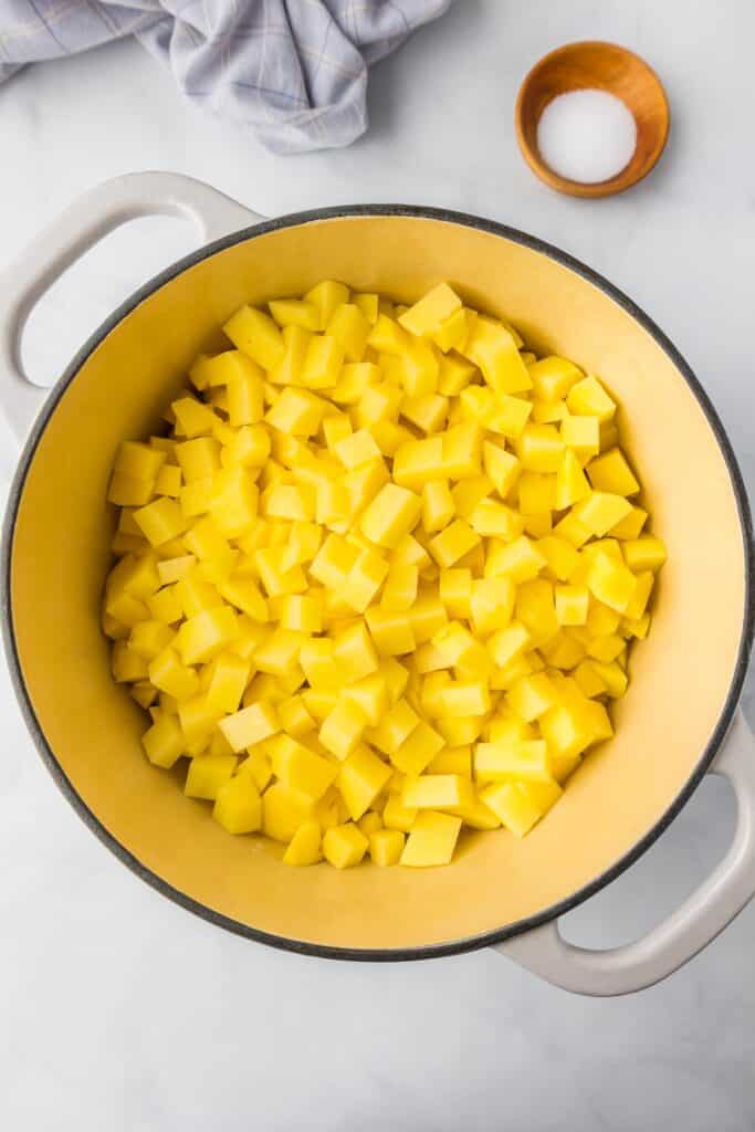 A large pot filled with diced yellow Yukon Gold potatoes with salt in a small bowl nearby on the counter.