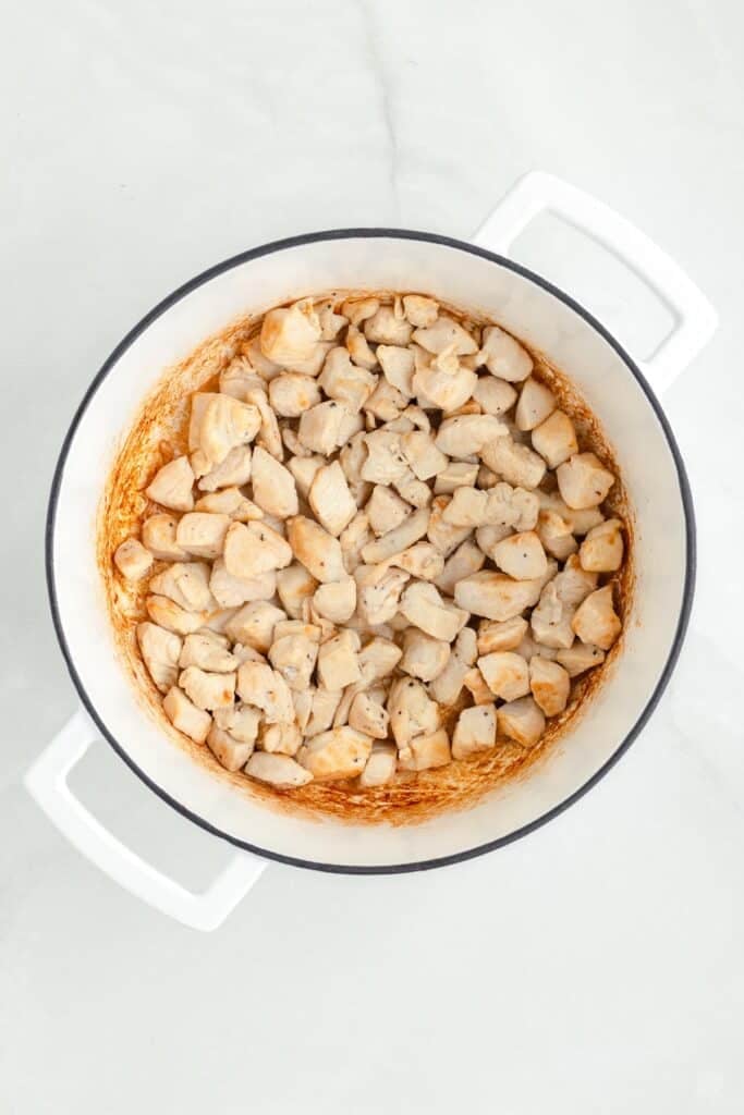 Cubed chicken pieces being browned in a white pot for chicken corn chowder.