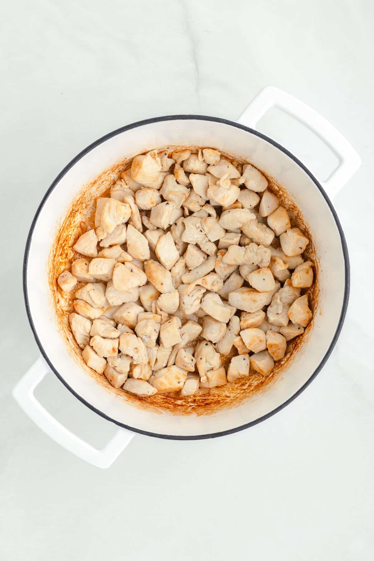 Cubed chicken pieces being browned in a white pot for chicken corn chowder.