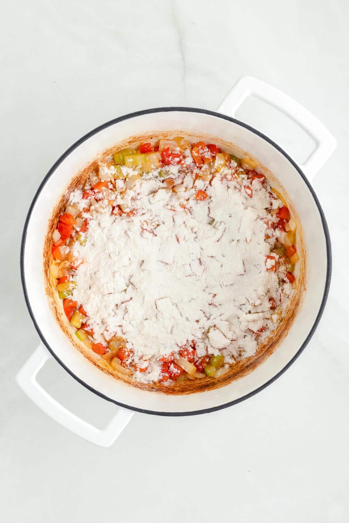 A large pot containing cooked chopped vegetables topped with flour being stirred into the vegetables for the roux of the chicken corn chowder.