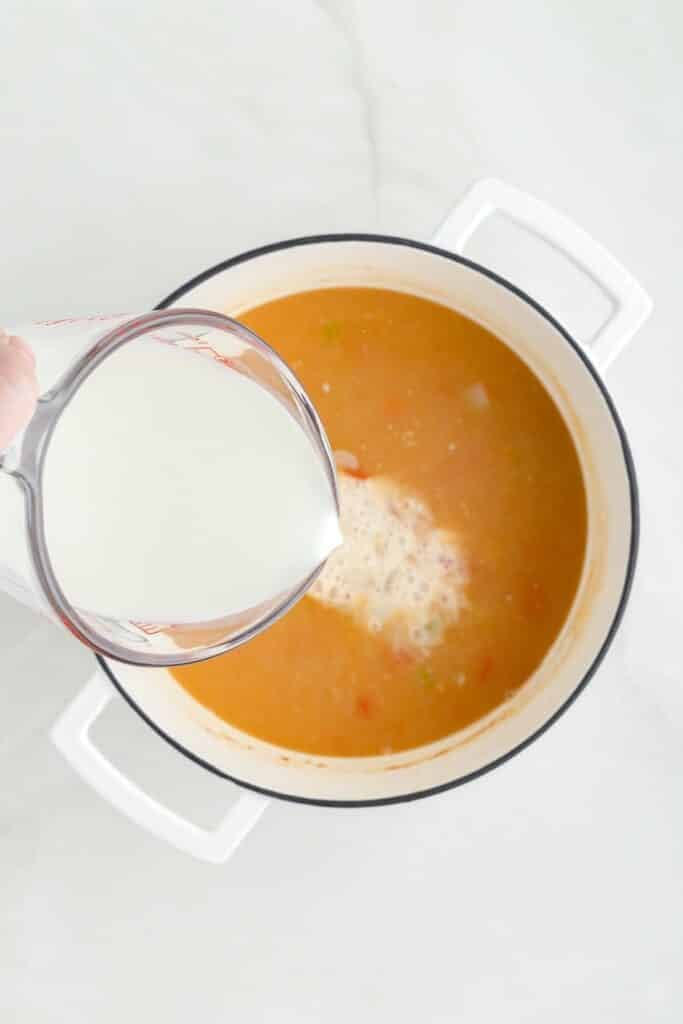 A measuring cup pouring milk into a pot of chicken corn chowder soup.
