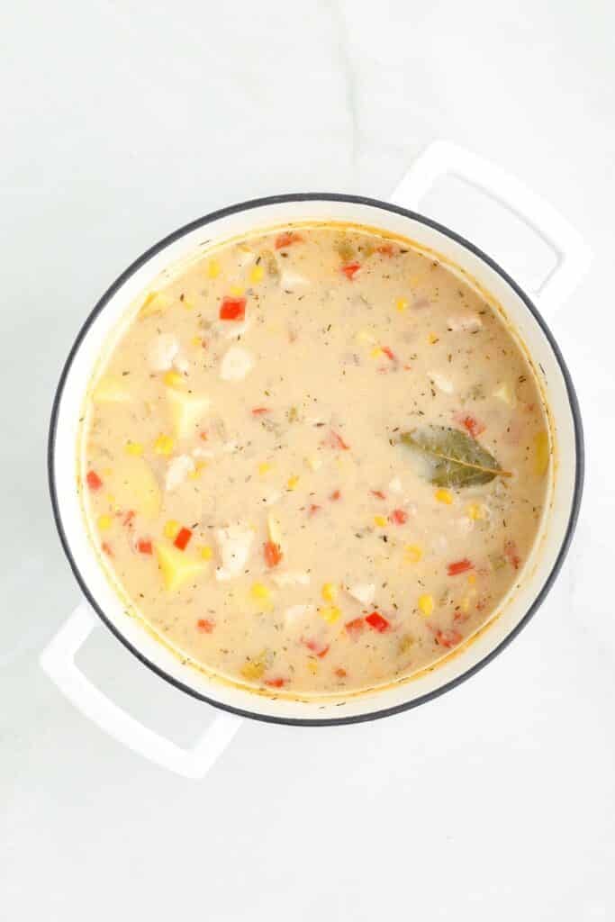 A pot of creamy chicken corn chowder after cooking with a bay leaf peaking out of the soup.