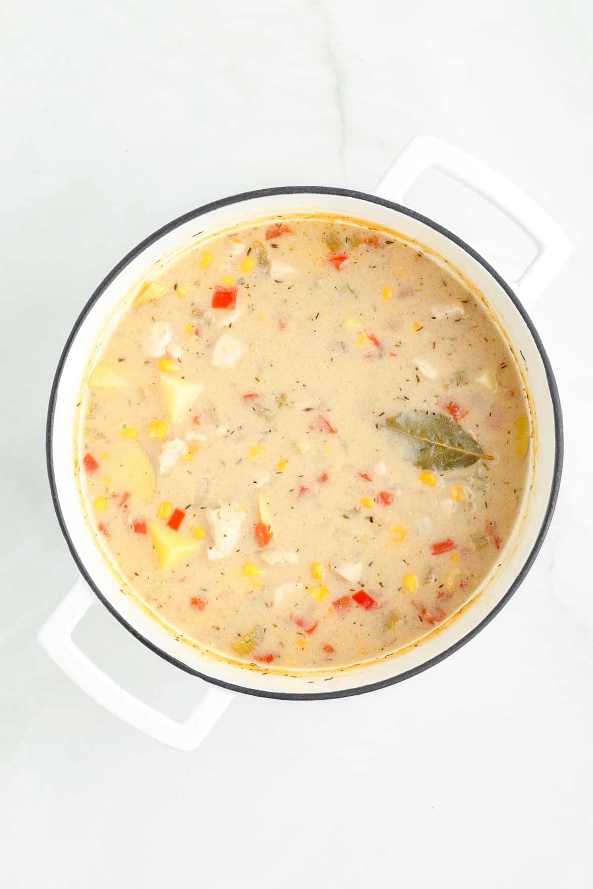 A pot of creamy chicken corn chowder after cooking with a bay leaf peaking out of the soup.