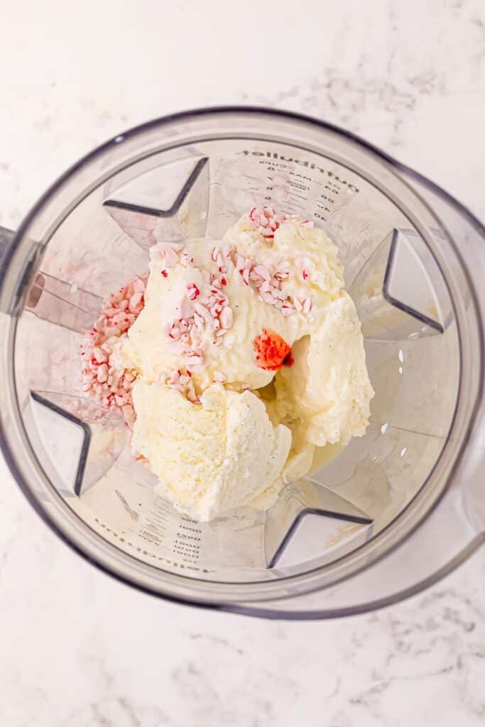 Vanilla ice cream, crushed peppermint, milk and red food coloring in a blender from overhead.