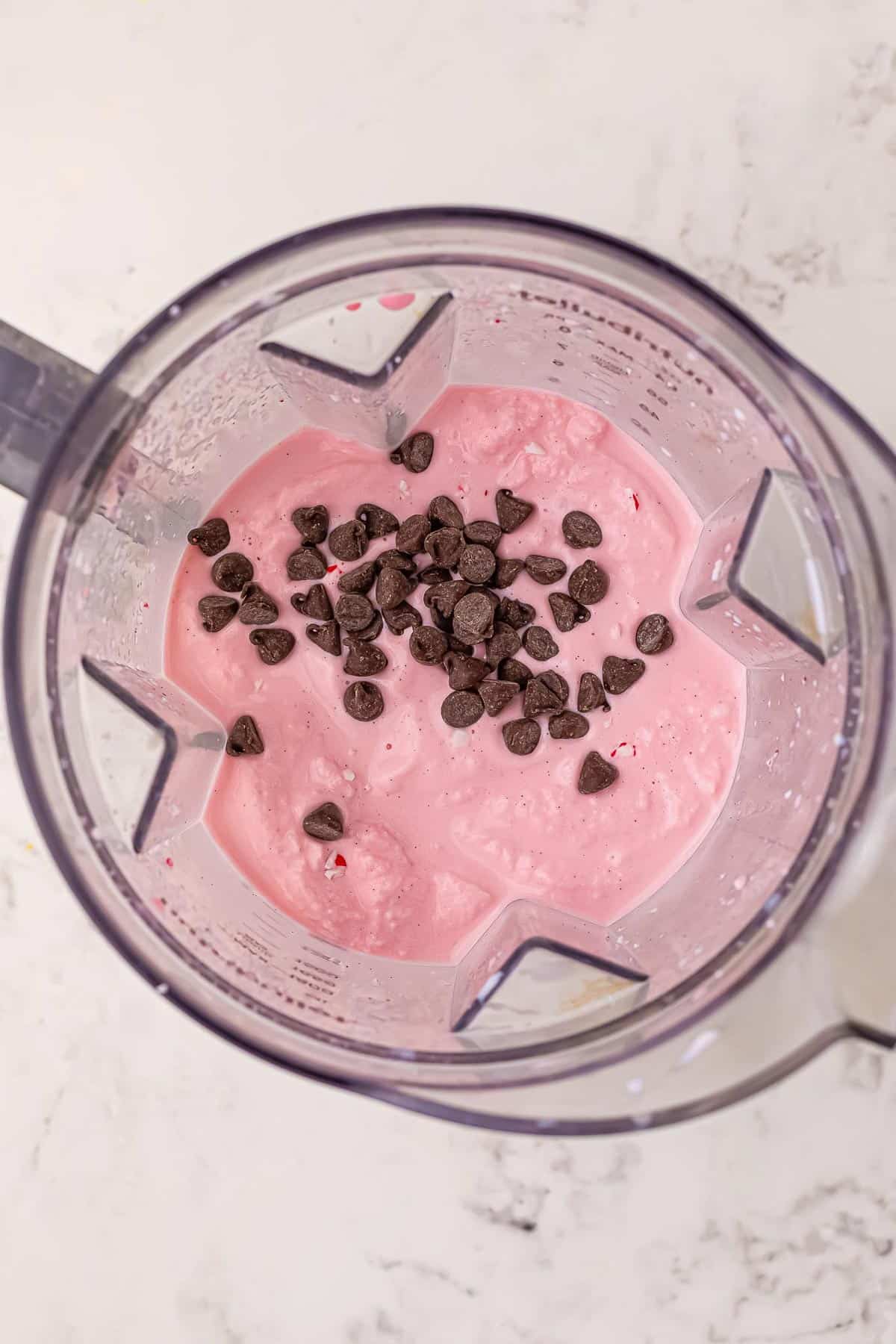 A blender from the top with chocolate chips being added to a peppermint milkshake.