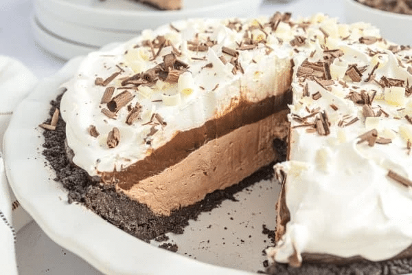 Chocolate pie with a slice removed, topped with whipped cream and chocolate shavings, in a white plate.