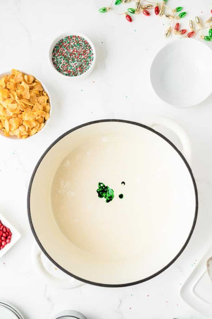 A pot full of a melted marshmallow mixture with green food coloring about to be mixed into the mixture.