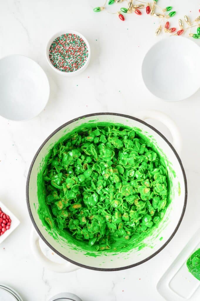 A pot full of a green marshmallow cornflake mixture sits near bowls of sprinkles.