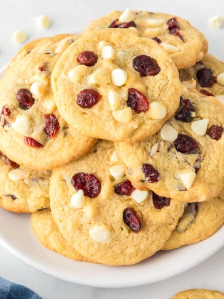 A square view of a plate of white chocolate chip cranberry cookies on a counter.