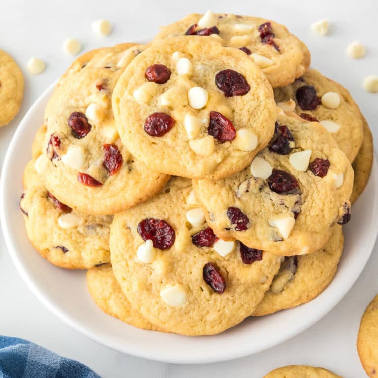 A square view of a plate of white chocolate chip cranberry cookies on a counter.