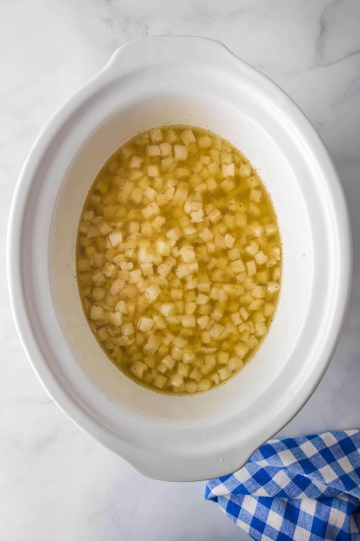 Diced potatoes in chicken broth in the base of a slow cooker for crock pot hash brown potato soup.