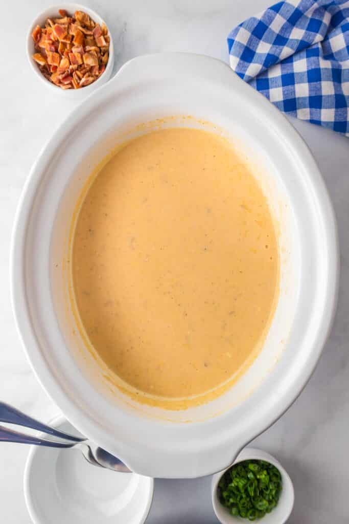 A crock pot filled with creamy crock pot hash brown potato soup after mixing in the cream cheese mixture on a counter.