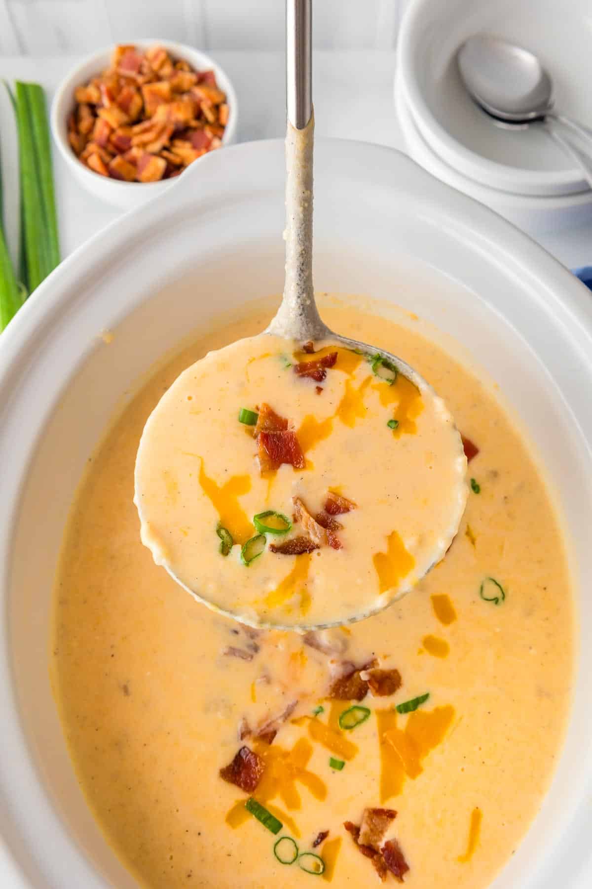 Close-up of a ladle scooping crock pot hashbrown potato soup from the base of a slow cooker.