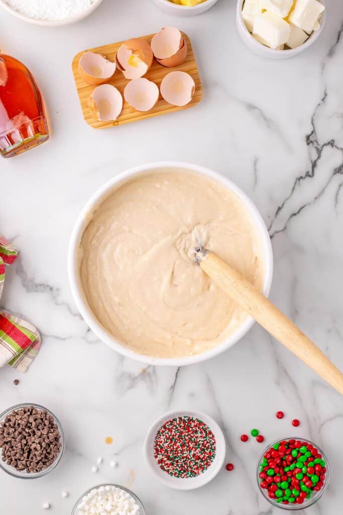 Bowl of elf cupcakes batter being mixed in a bowl from above with other ingredients for toppings nearby.