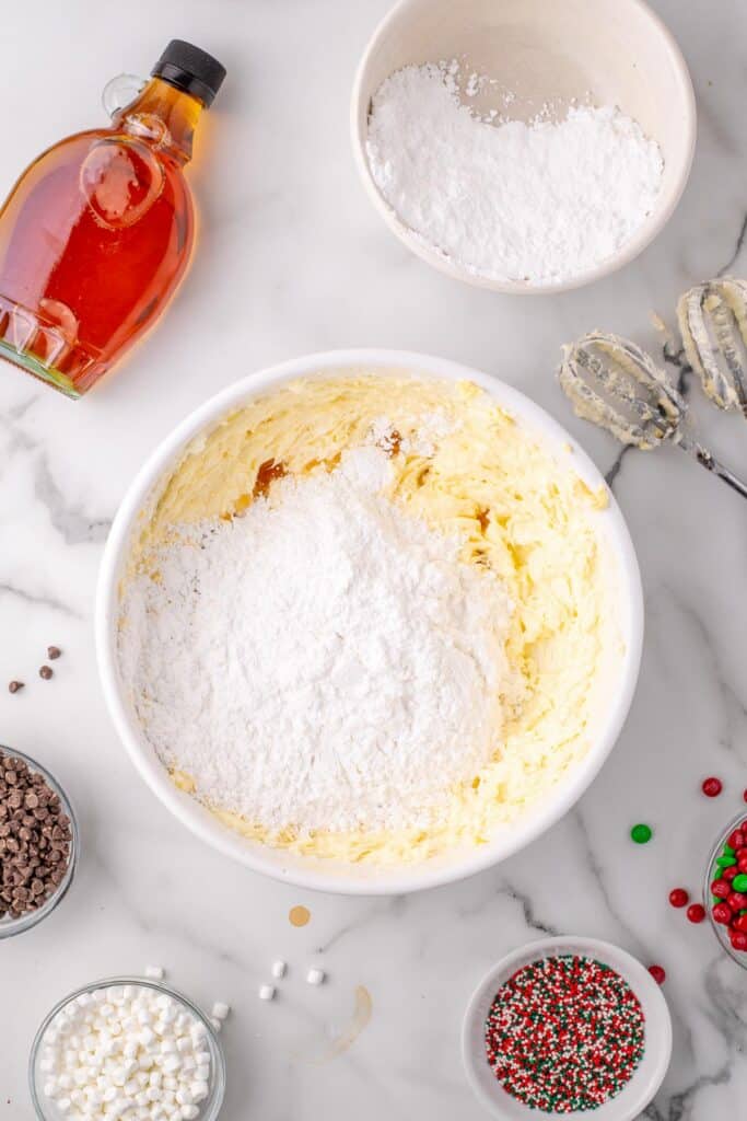 Powdered sugar being added to butter and shortening mixture for frosting in a bowl to top Elf cupcakes.