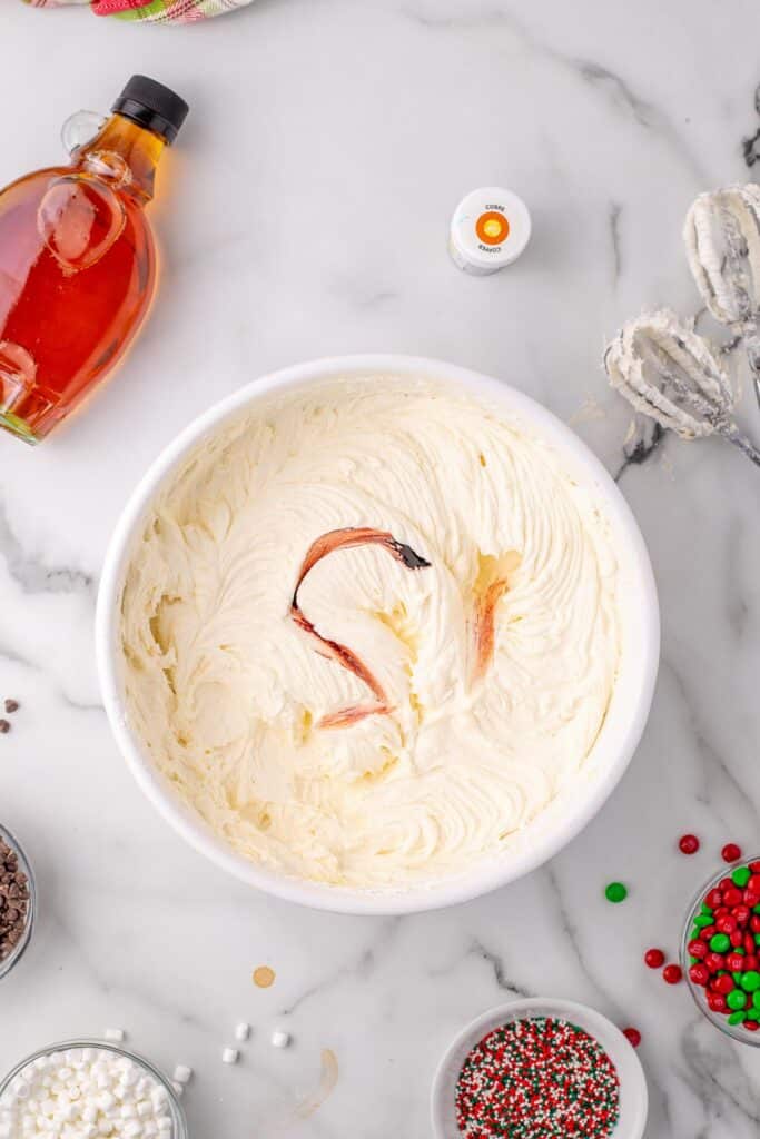 A mixing bowl full of frosting for elf cupcakes with food coloring being mixed in to make the frosting yellow.