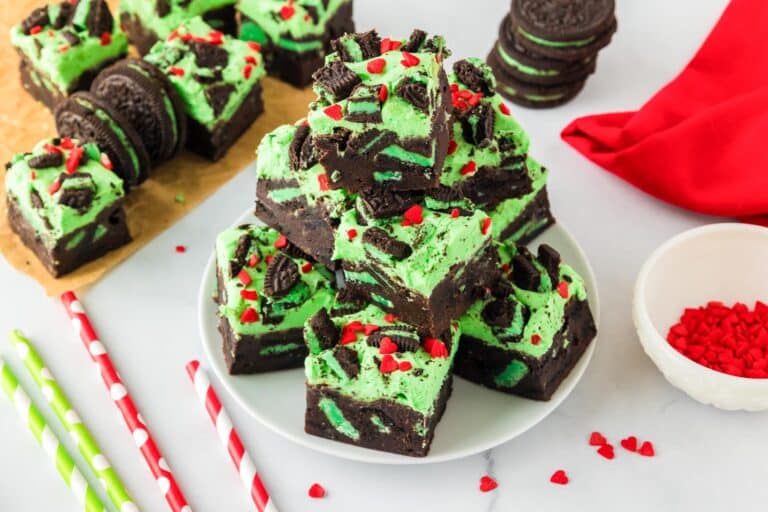 stack of green mint frosted chocolate Grinch brownies topped with crushed mint Oreo cookies and red heart sprinkles.