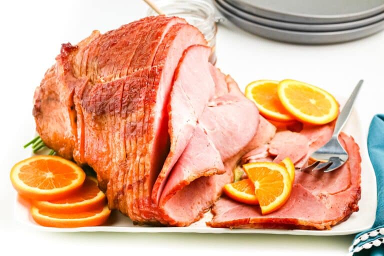 Sliced glazed ham on a large platter from the side with orange slices.