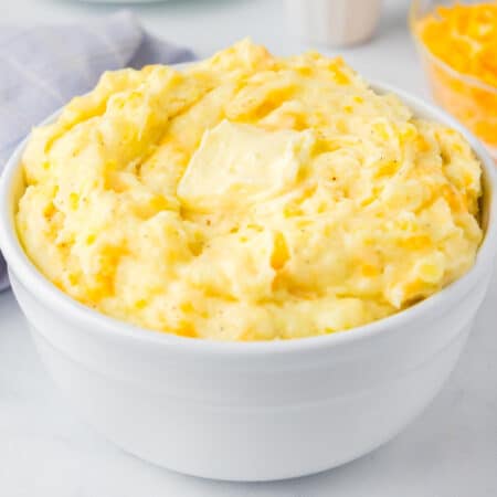 A square view of a large bowl filled with Yukon Gold mashed potatoes topped with a melty pat of butter.