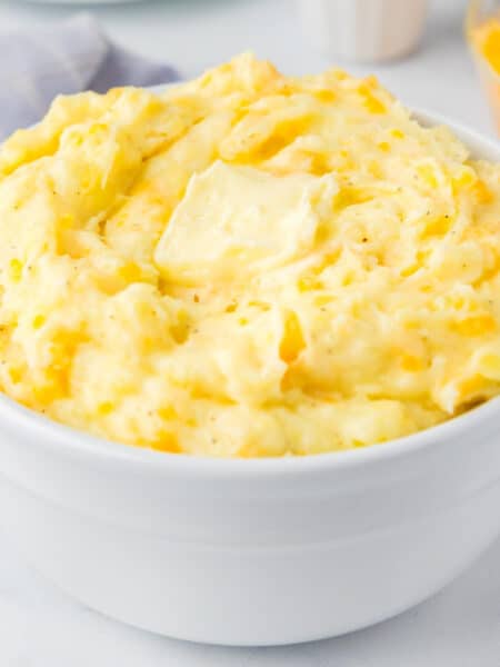 A square view of a large bowl filled with Yukon Gold mashed potatoes topped with a melty pat of butter.