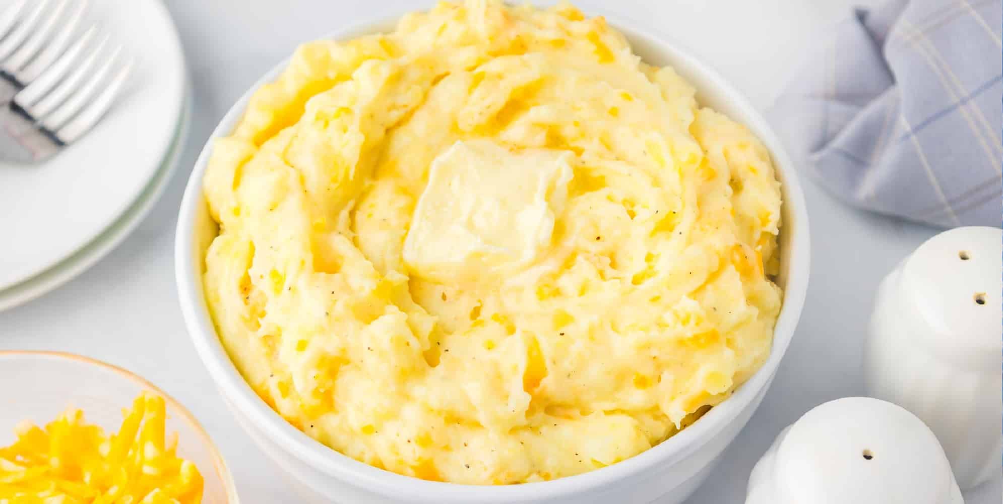 Wide view of a bowl of Yukon Gold mashed potatoes with a pat of melty butter on top on a dinner table.