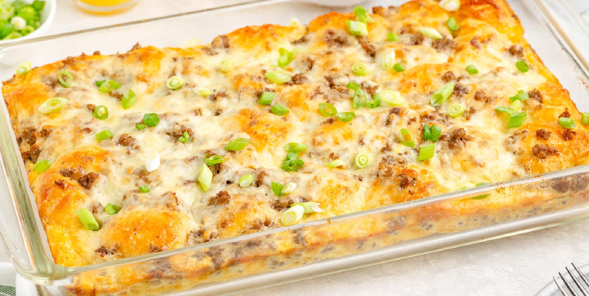 A wide view of a breakfast biscuit casserole with golden brown biscuit pieces, gooey cheese, egg and pieces of sausage.