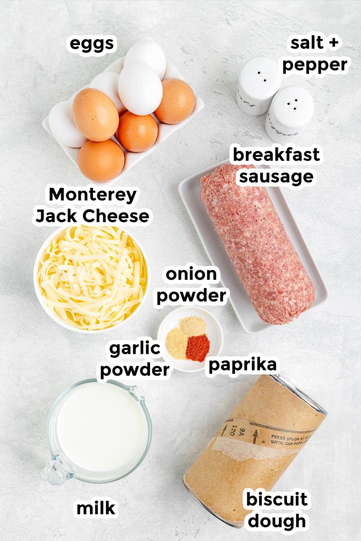 Ingredients for a breakfast biscuit casserole in bowls on a counter with text labels.