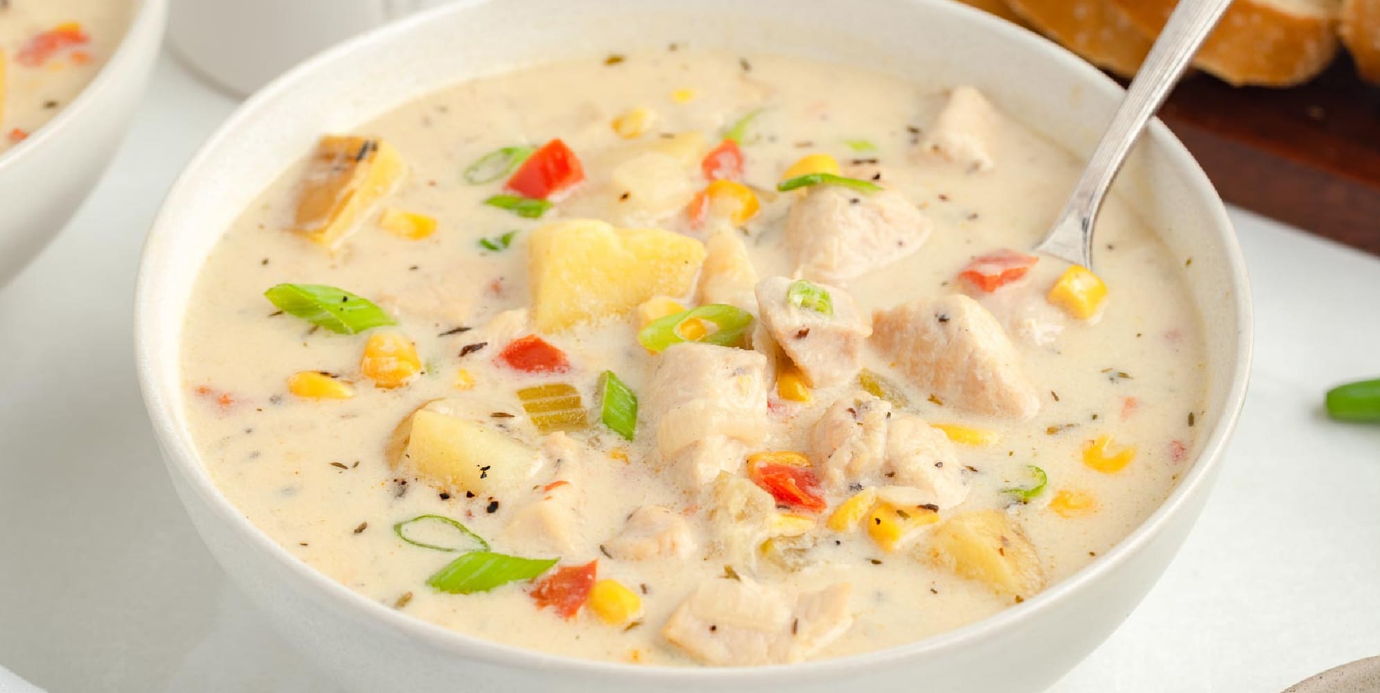 A wide view of chicken corn chowder in a bowl being scooped by a spoon.