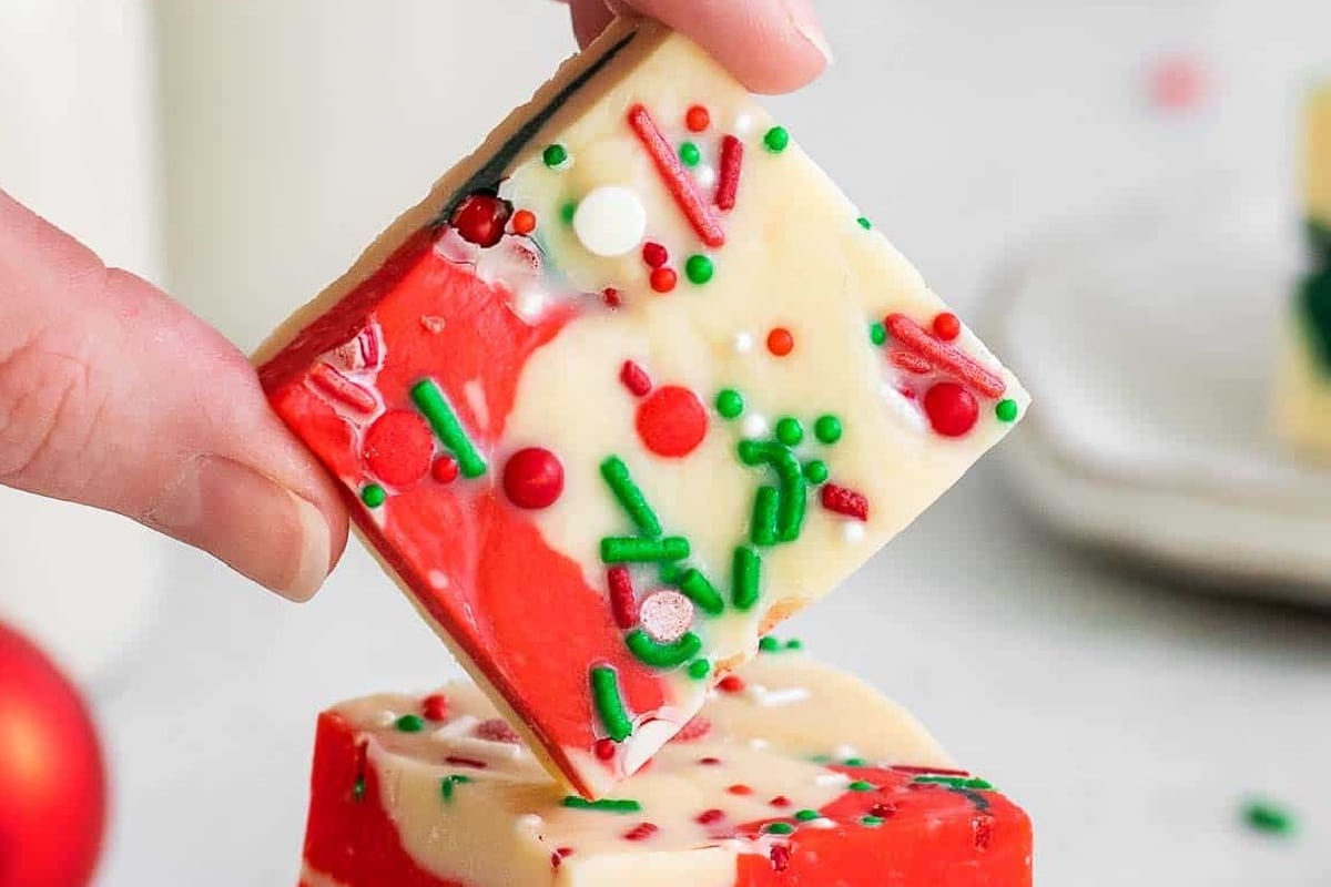 A hand holds a square of red and white sprinkles topped in sprinkles.