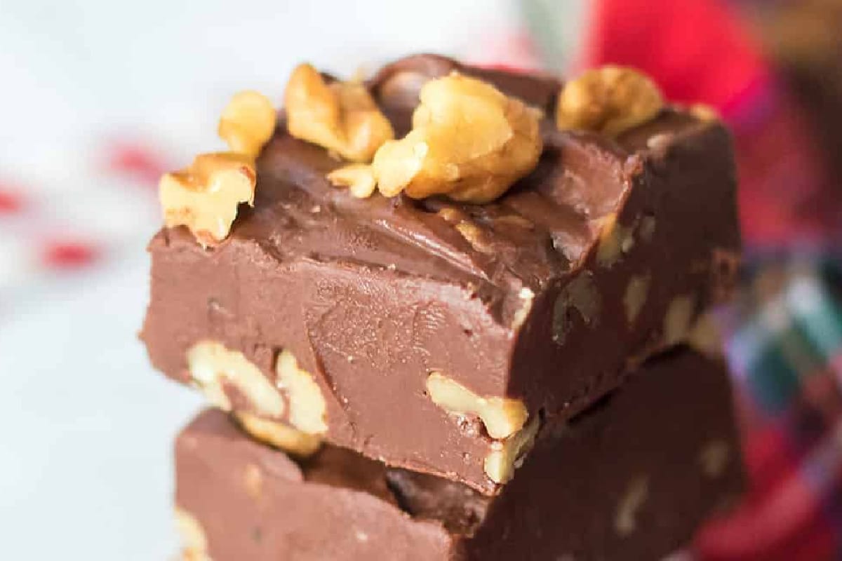 Two pieces of chocolate coca cola nut fudge stacked on each other, topped with walnut pieces.