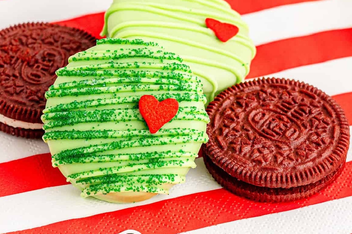 Green chocolate dipped Oreo cookies with red heart decorations and two red velvet oreos nearby on the napkin.