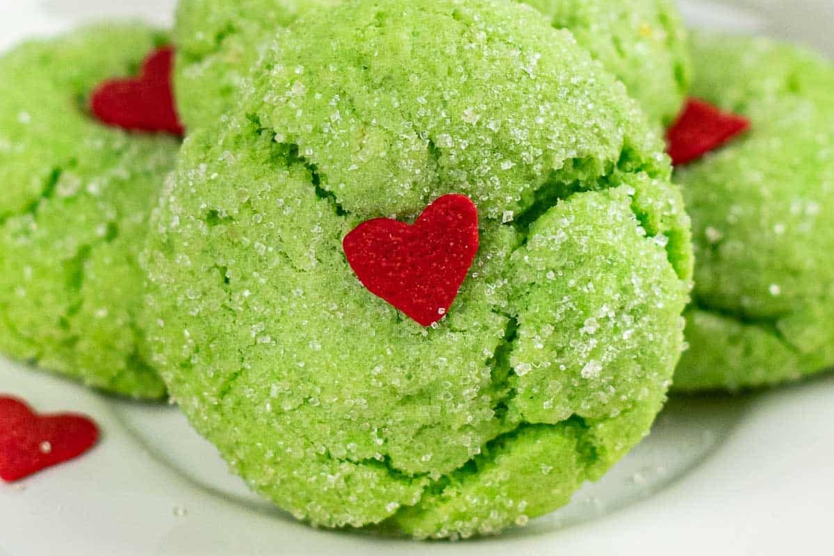 Green crinkle Grinch sugar cookies with red heart decorations on a plate.