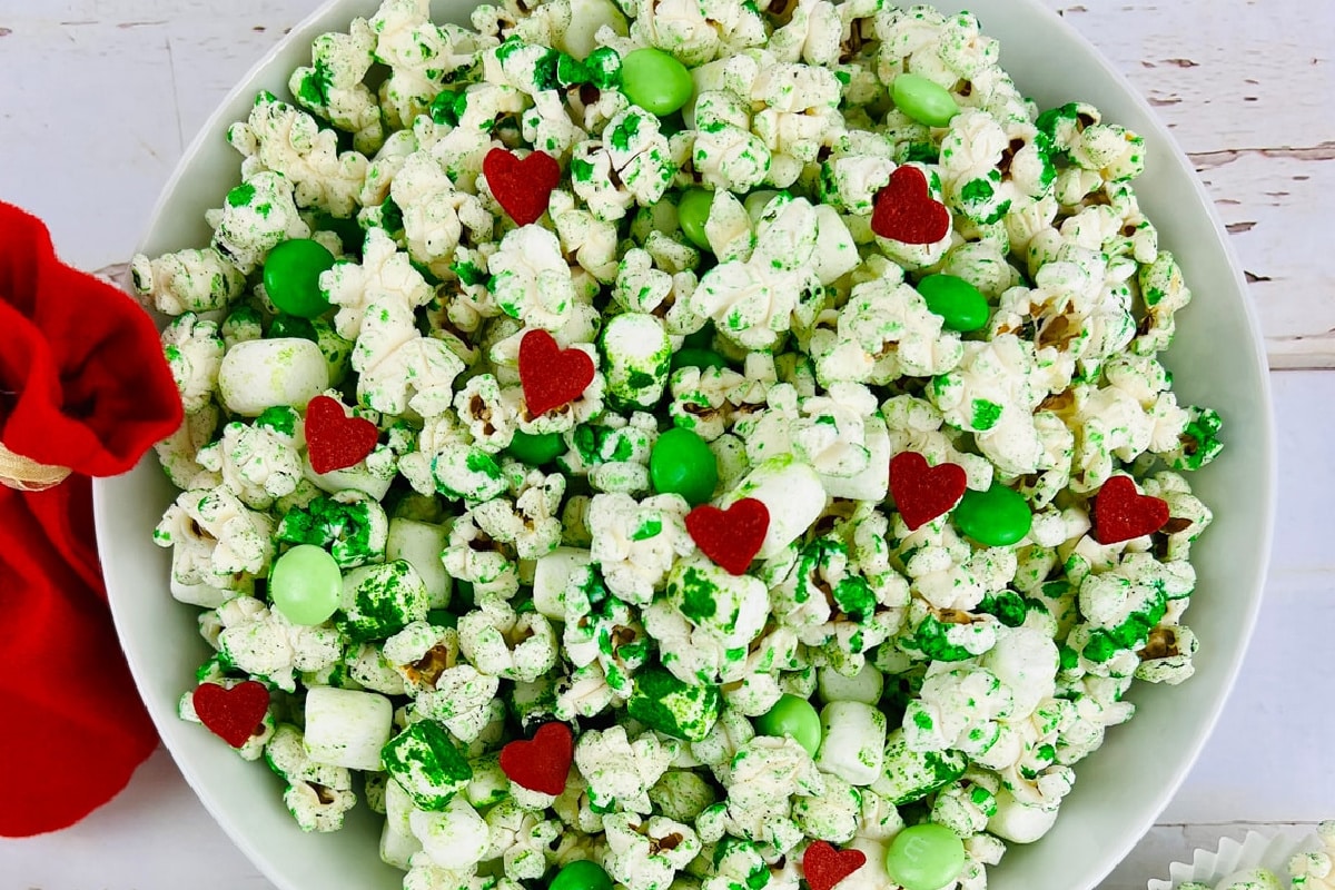 A bowl of green Grinch popcorn mixed with green candy-coated chocolates, small green candies, and heart-shaped red in a bowl.