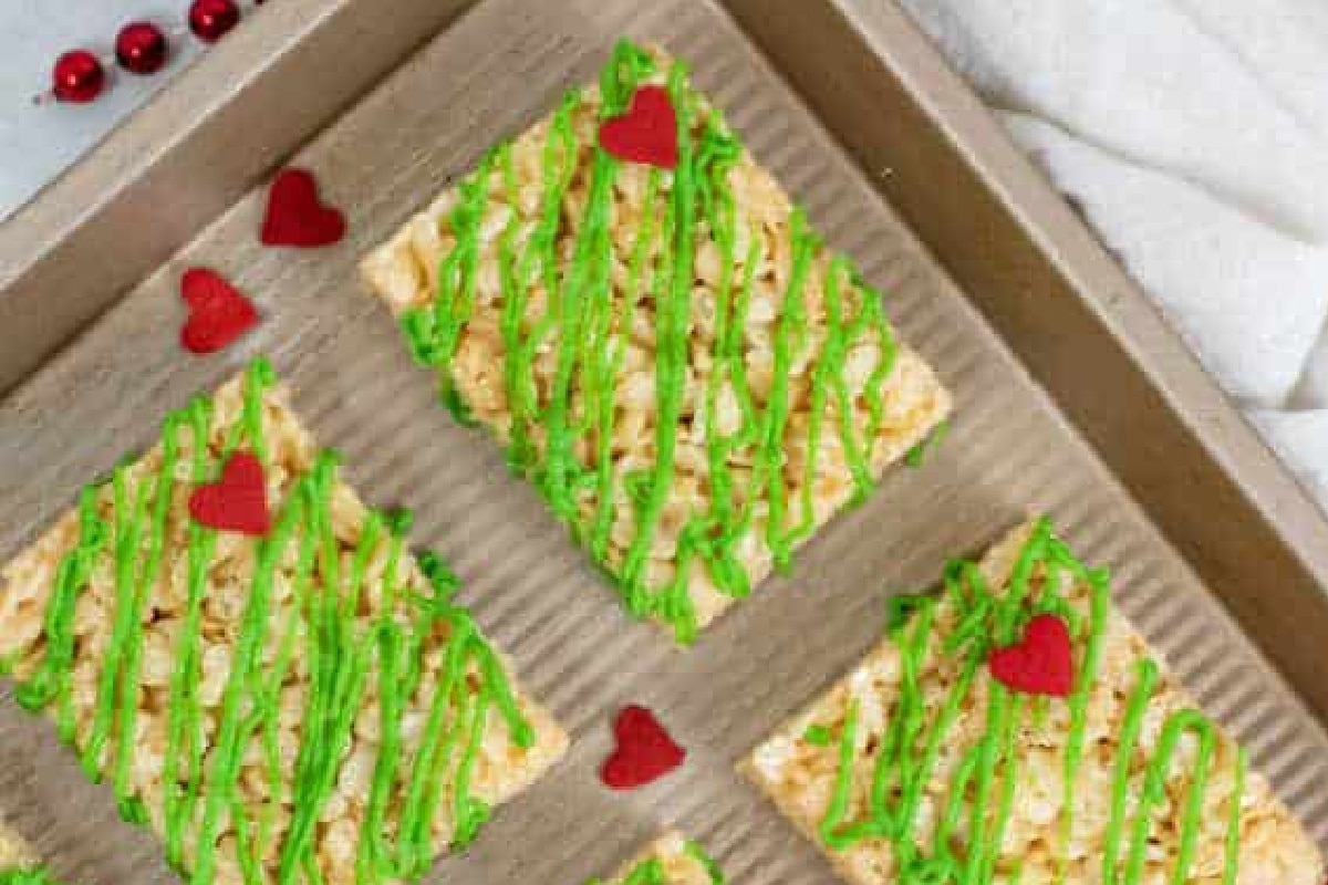 Rice Krispie treats with green Grinch icing drizzles and red heart decorations on a baking tray.