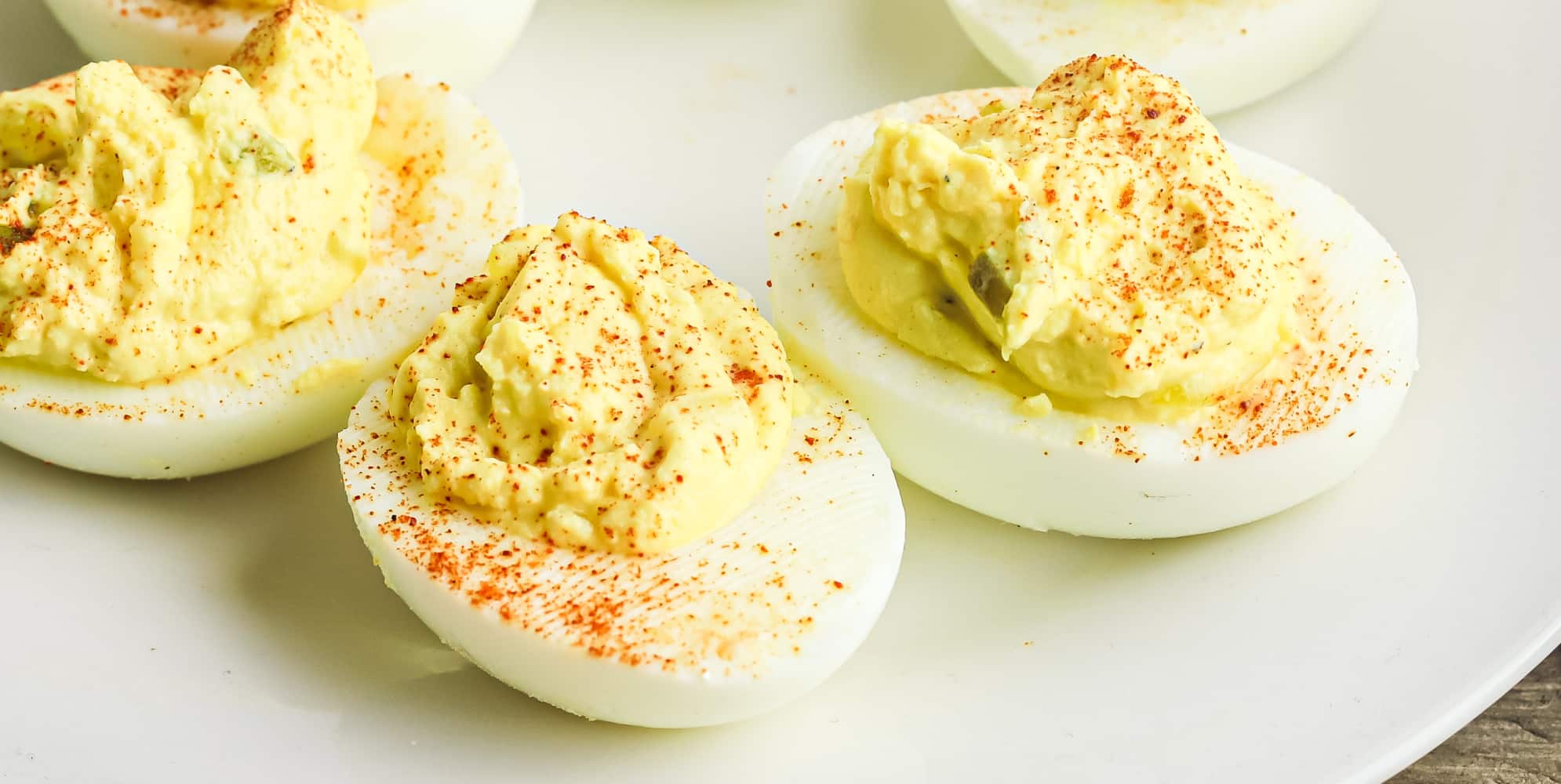 A plate of three deviled eggs topped with paprika.