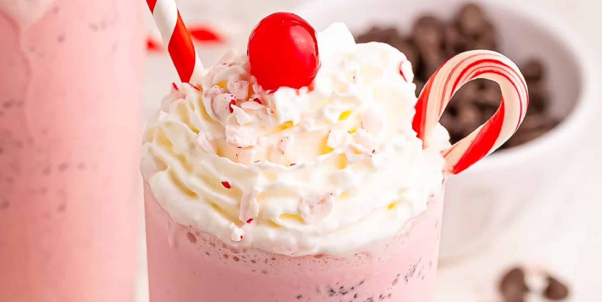 A wide view of the top of a pink copycat chick fil a peppermint milkshake topped with whipped cream, a cherry, and a candy cane.