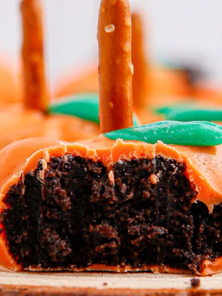 Close-up of orange candy chocolate pumpkins with pretzel stems and green leaves with one missing a bite.